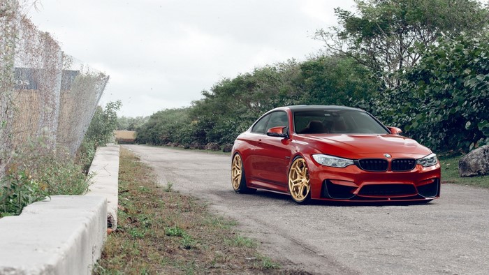 Red BMW M4 with gold wheels on a dirt road