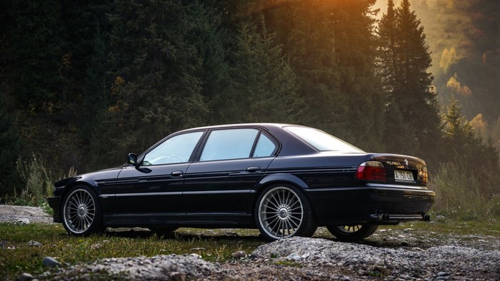 Black BMW Alpina E38 sedan in a forest