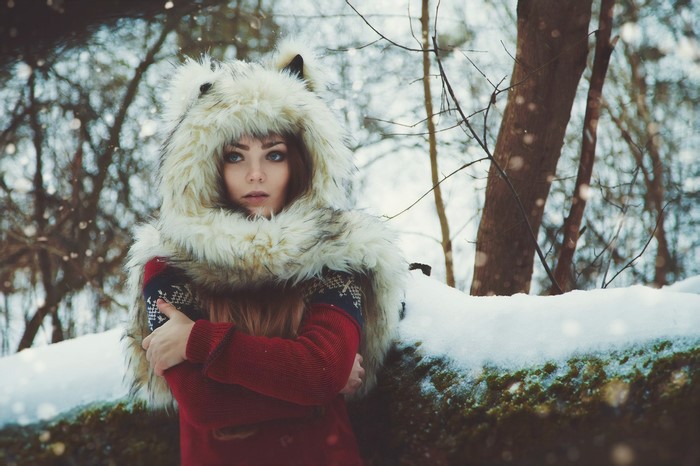 Woman in wolf hat and red sweater in winter forest