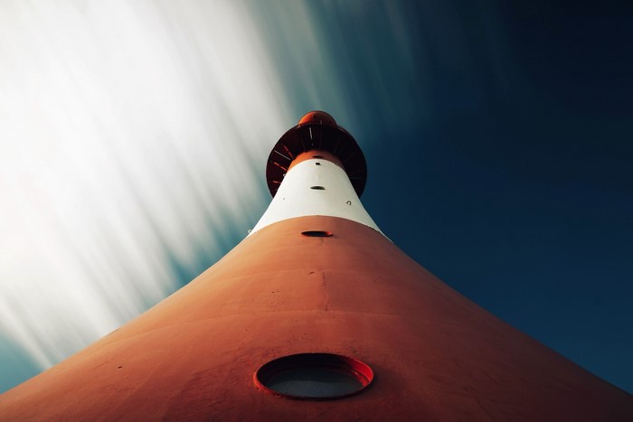 Worms eye view of a red and white lighthouse against a streaky sky