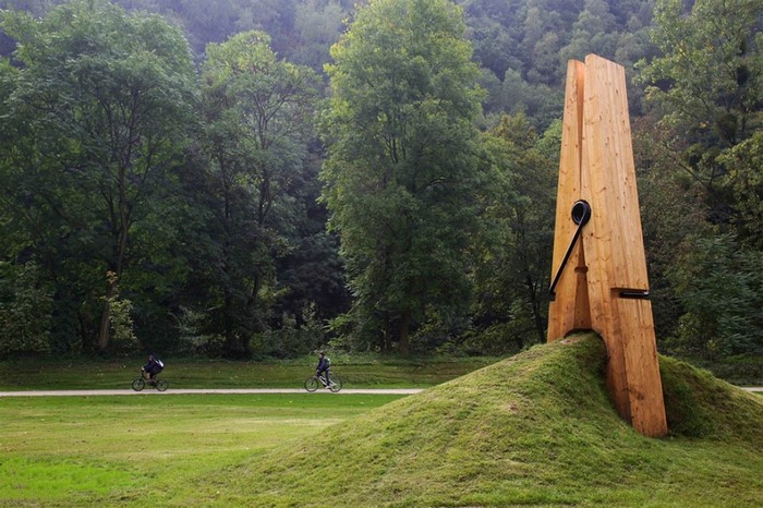 Giant wooden clothespin sculpture in a park with cyclists