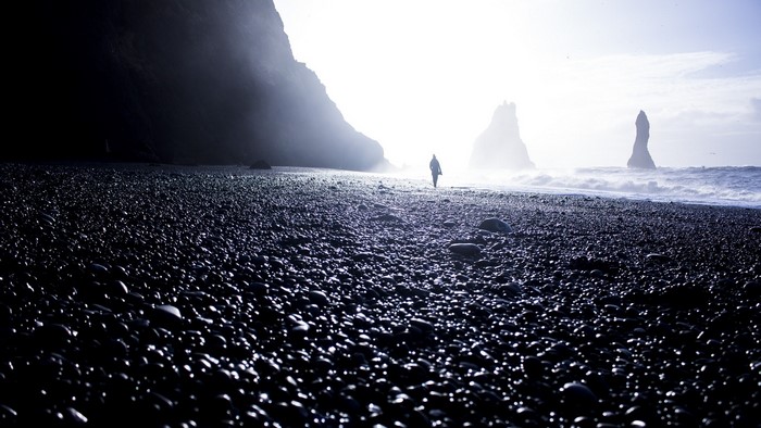 Person walking on Reynisfjara black sand beach, Iceland