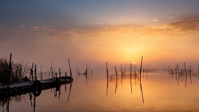 Calm lake with pier and fishing nets at sunset