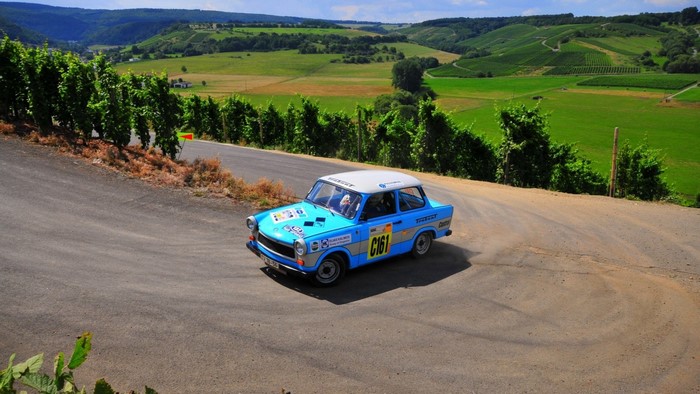 Blue Trabant rally car on a winding road with vineyards