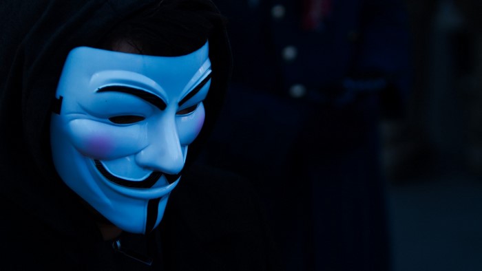Person wearing a blue Guy Fawkes mask and hood
