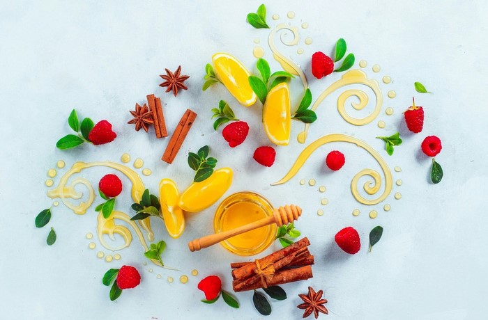 Honey, raspberries, oranges, cinnamon, and star anise on a light background