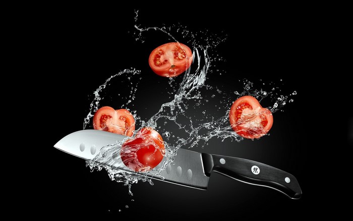 Knife slicing tomatoes with water splash