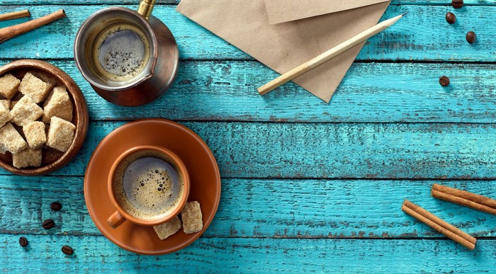Coffee, sugar cubes, cinnamon sticks, and envelope on turquoise wood