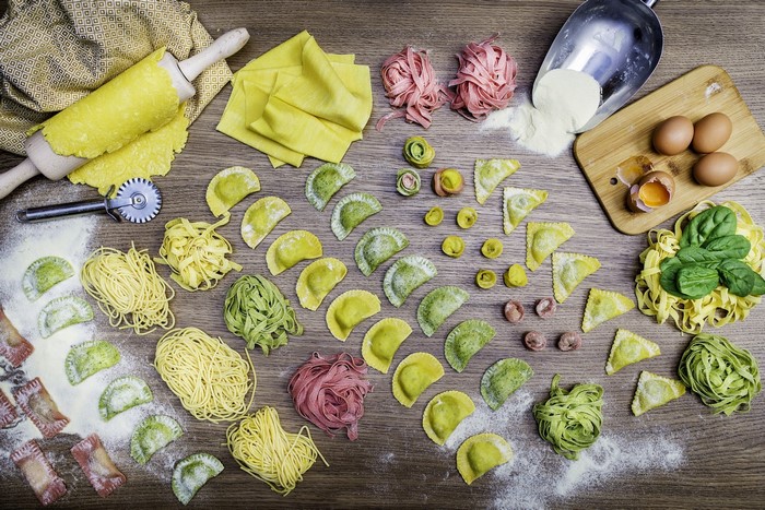 Various pasta shapes, eggs, and flour on a wooden table