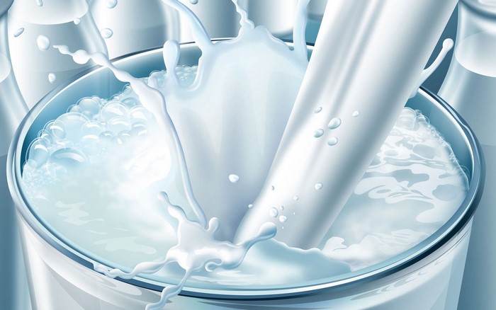 Milk splashing into a glass with bottles in background
