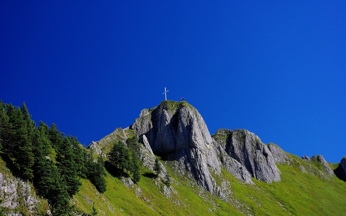 Cross on a rocky mountain peak with green slopes