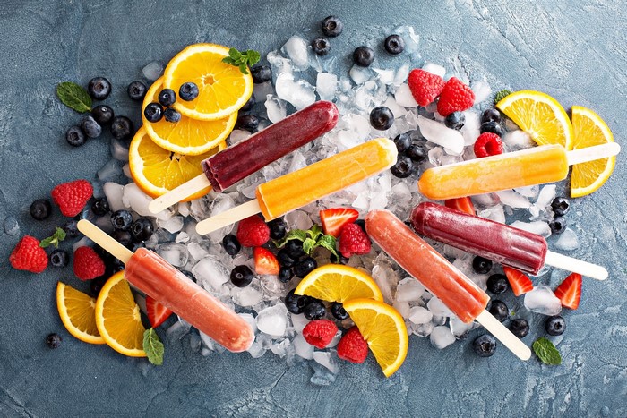 Assortment of fruit popsicles with berries and orange slices on ice