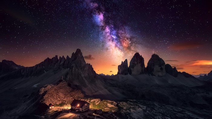 Milky Way over Dolomites mountains with illuminated buildings