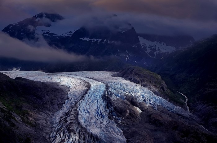 Glacier winding through mountains under clouds