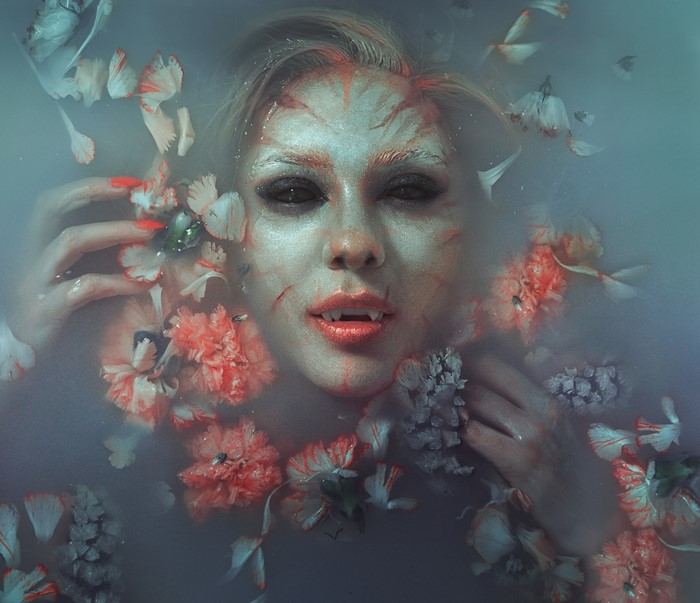 Vampire woman with fangs in water with flowers