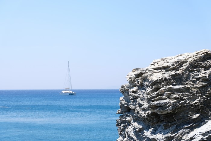 Catamaran sailing in the blue sea near a rocky shore