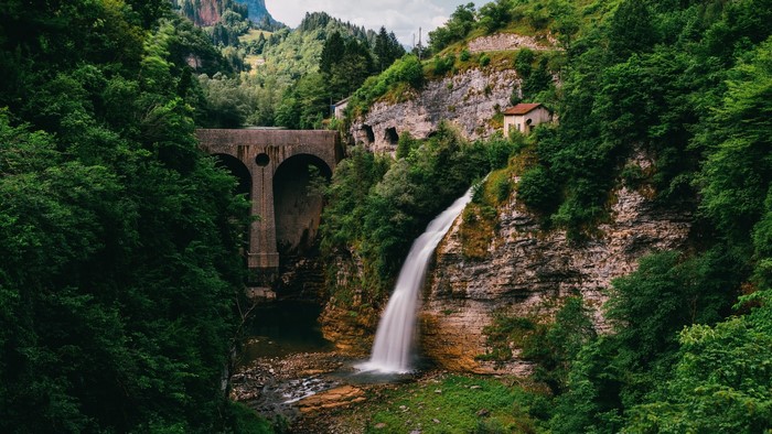 Waterfall cascading near a stone bridge in a green mountainous landscape