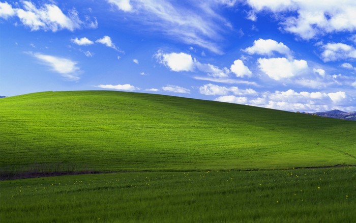 Rolling green hill under a blue sky with clouds