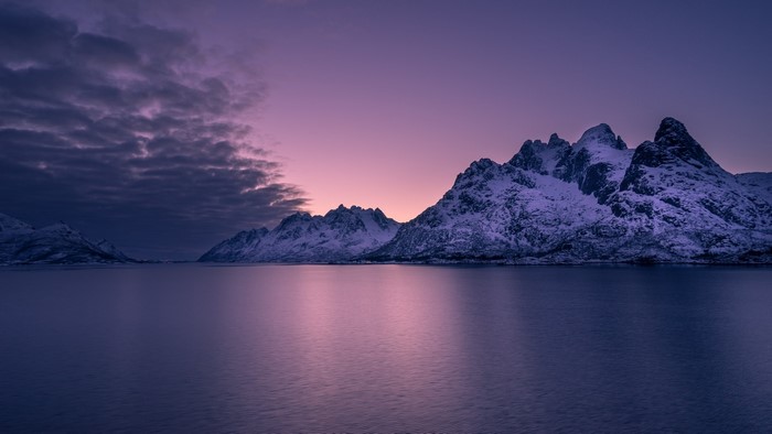 Snowy mountains at sunset over a calm sea