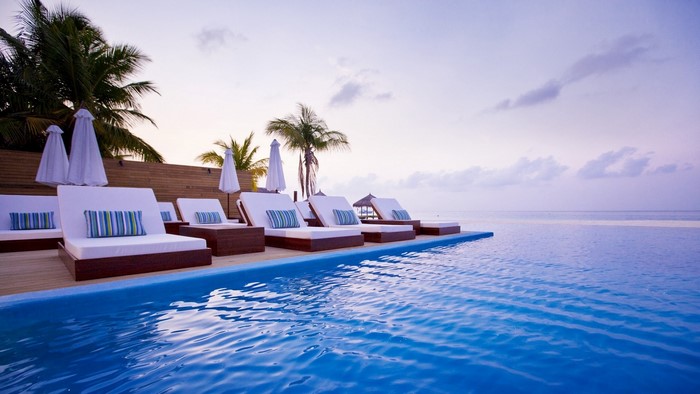 Infinity pool and lounge chairs at sunset in the Maldives