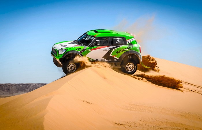 Green Mini Countryman rally car jumping over sand dunes