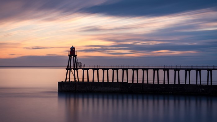 Pier with lighthouse at sunrise with long exposure clouds