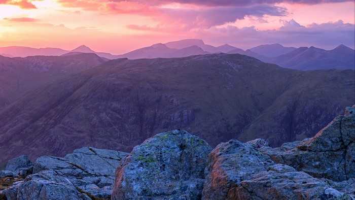 Purple mountains at sunset with rocks in foreground