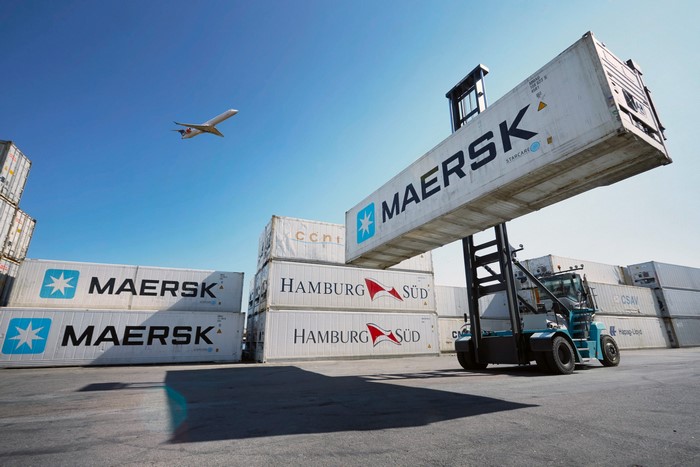Maersk containers being moved by a forklift with an airplane overhead