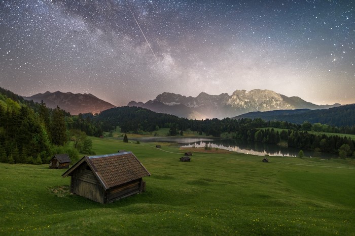 Wooden cabins in a grassy field under the Milky Way