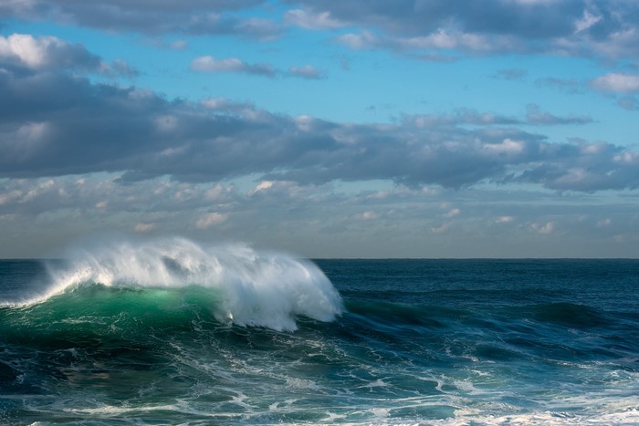 Crashing wave in the Pacific Ocean under cloudy sky