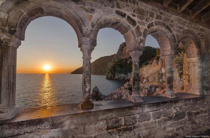 Sunset over the sea viewed through ancient stone arches in Italy