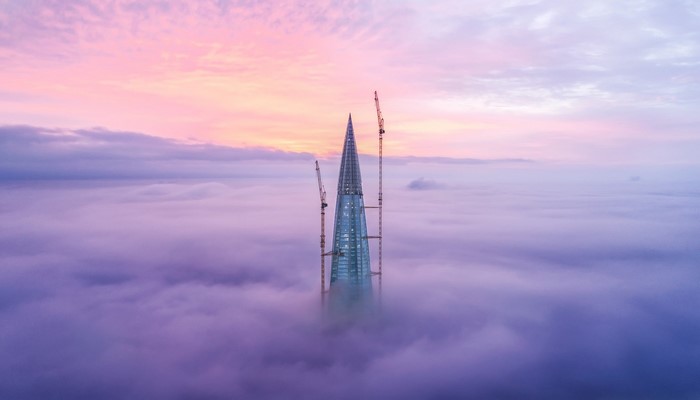 Skyscraper under construction above clouds at sunrise
