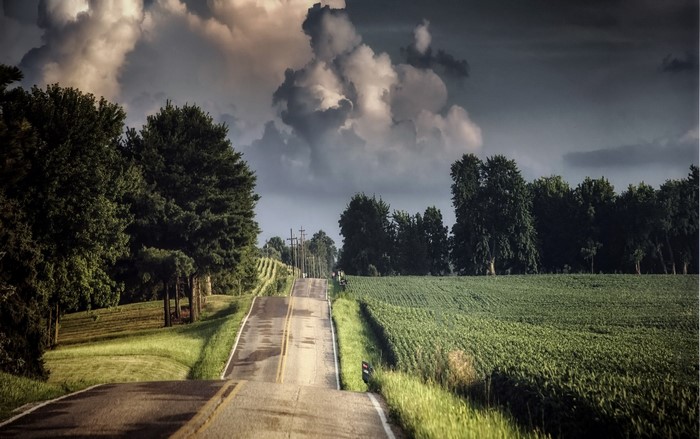 A Winding Road Through Rural Fields Under Stormy Clouds