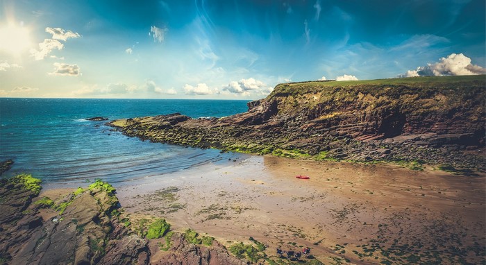 Red kayak on a sandy beach with rocky cliffs and the sea