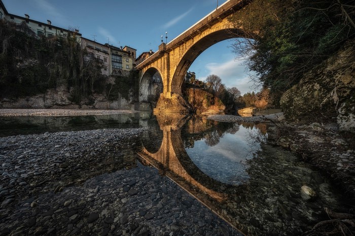 Stone bridge over a river with reflections in Italy