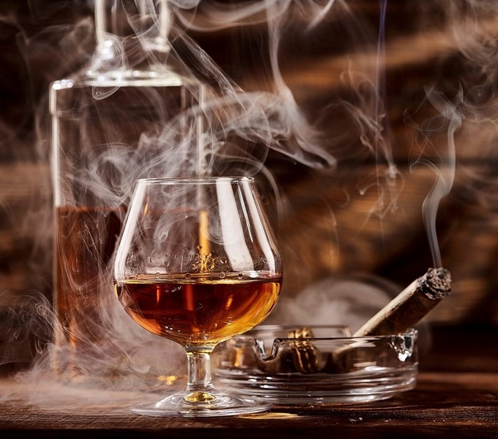 Cognac bottle, glass, and smoking cigar with smoke