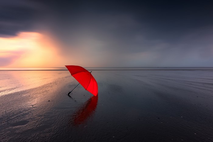 Red umbrella on a wet beach at sunset