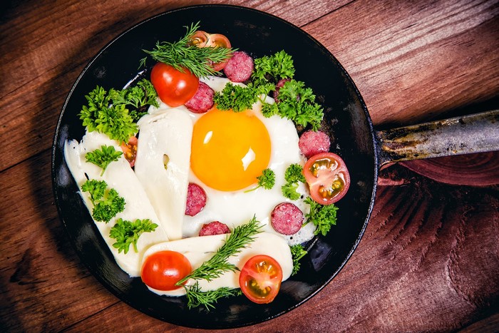 Fried egg with cheese, tomatoes, and sausage in a pan