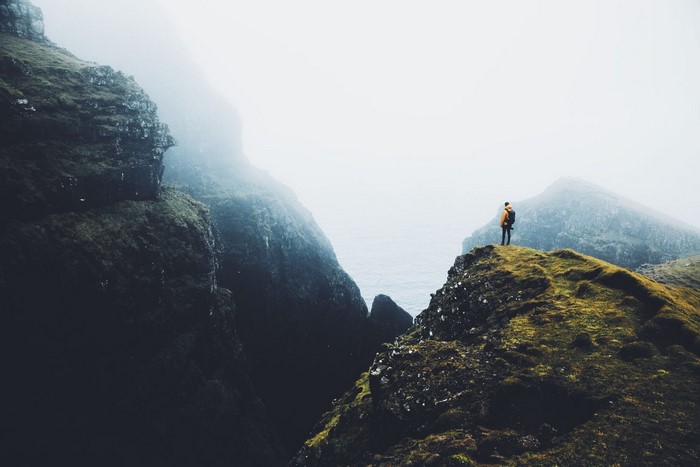 Man standing on a cliff overlooking a misty landscape