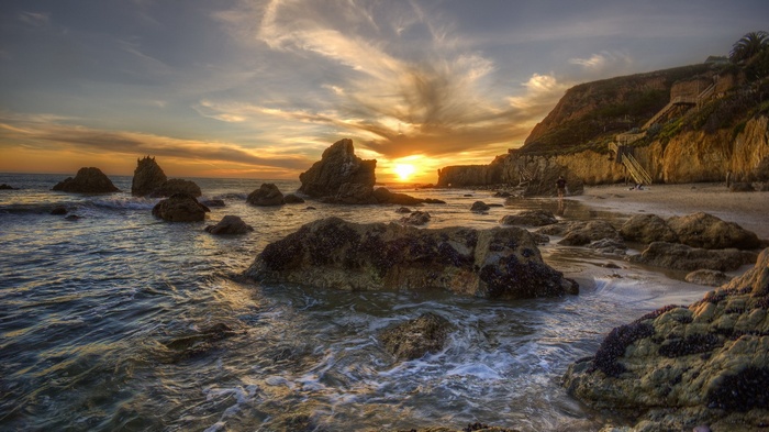 Sunset over rocky beach with cliffs and stairs