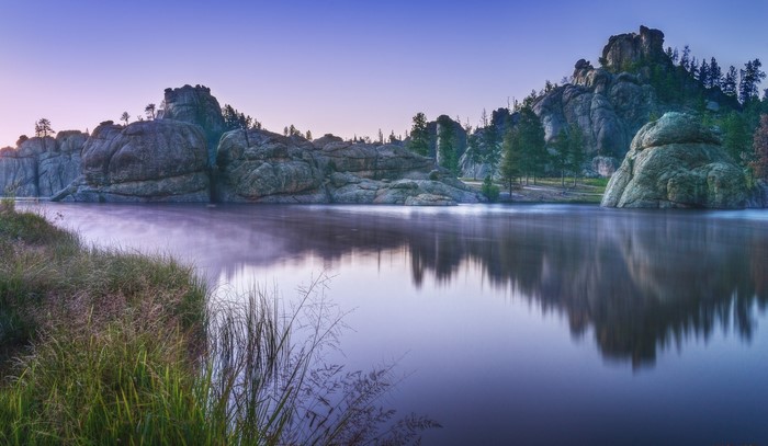 Misty lake with rock formations and trees at sunrise