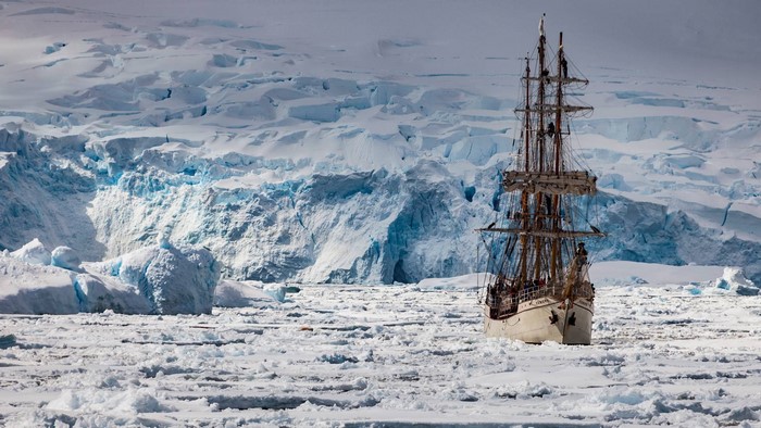 Tall ship sailing through icy waters near a glacier