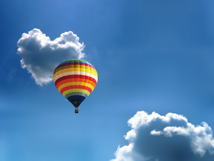 Hot air balloon near heart-shaped cloud in blue sky
