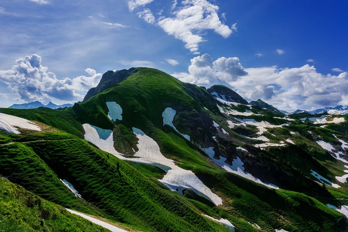 Green mountains with snow patches under a blue sky