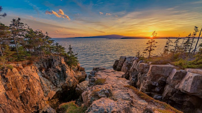 Rocky coastline at sunset with ocean and distant hills