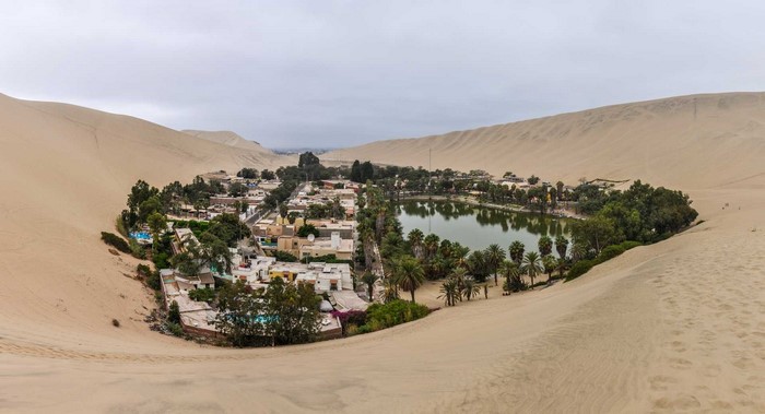 Oasis village with lake and palm trees surrounded by sand dunes in Peru