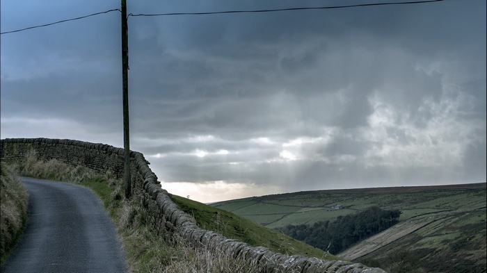 Winding country road with stone walls and stormy sky