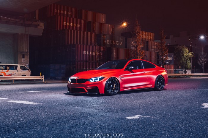 Red BMW M4 parked at night near shipping containers