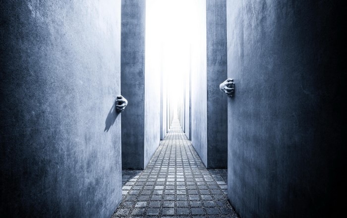 Hands emerging from concrete pillars in a surreal pathway