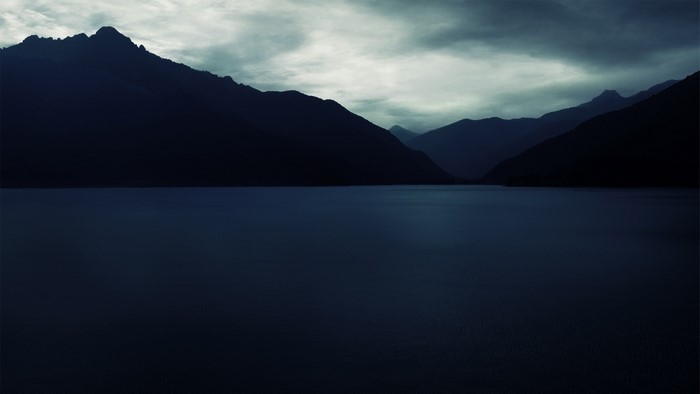 Dark mountains over a lake under cloudy sky